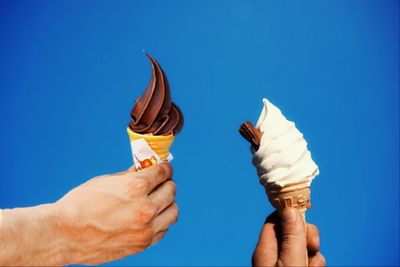 Cropped image of hand holding ice cream against blue sky