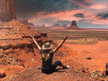 Rear view of woman sitting with arms raised on land against sky