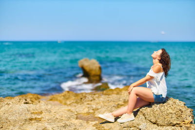 Young woman sitting on rock at beach