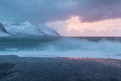 Scenic view of sea by snowcapped mountains against sky during sunset