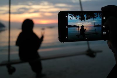 Rear view of silhouette people photographing sea against sky during sunset