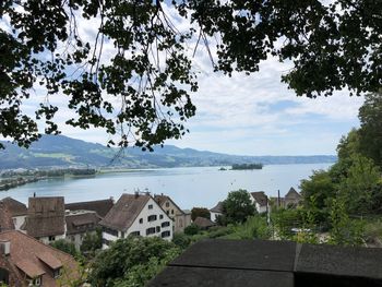 Houses and trees by lake against sky in city