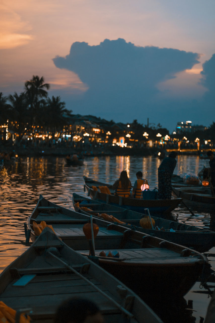 PEOPLE SITTING ON BOATS MOORED IN SEA AT DUSK