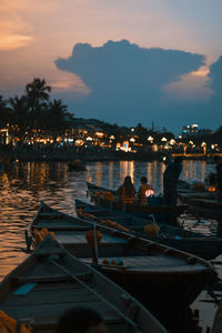 People sitting on boat moored in sea against sky at sunset