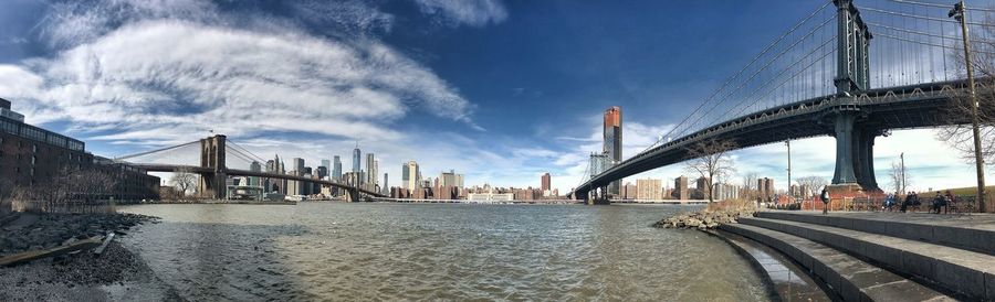 Suspension bridge over river against sky in city