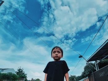 Low angle portrait of boy standing against sky