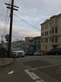 Cars on street by buildings in city against sky