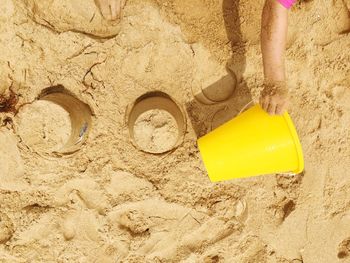 Cropped image of child playing with yellow bucket on sand at beach