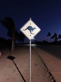 Road sign by trees against clear blue sky