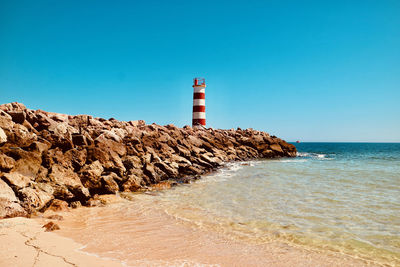 Lighthouse by sea against clear blue sky