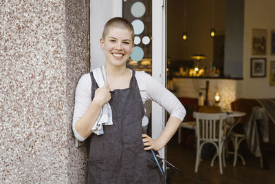 Portrait of young happy female cafe owner with hand on hip standing at doorway