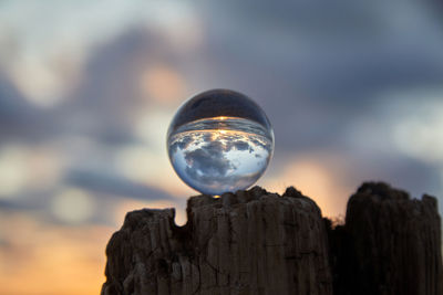 Close-up of crystal ball on wooden post against sky