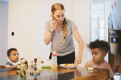 Mother talking on mobile phone while standing by children at table