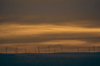 Windmills on field against cloudy sky during sunset