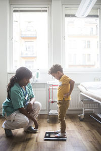 Mature doctor looking down while boy standing on weighing scale in clinic