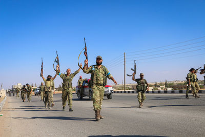 Soldiers holding gun walking on road against sky