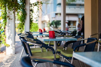 Empty chairs and tables at sidewalk cafe amidst buildings