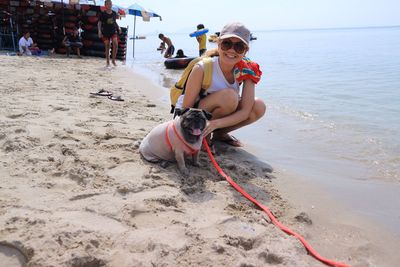 Portrait of smiling woman crouching by dog at beach