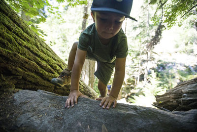 Young boy hiking, scrambling over large rock.