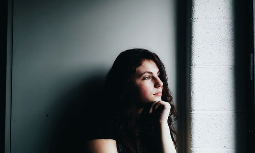 Portrait of beautiful young woman sitting against wall