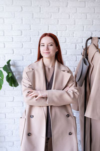Beautiful young woman in beige coat standing in front of hanger rack and choosing outfit dressing. 