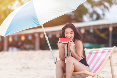 Young woman sitting on swing while holding umbrella