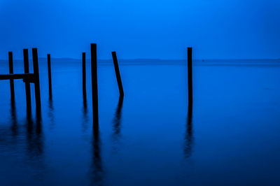 Wooden posts in sea against clear blue sky