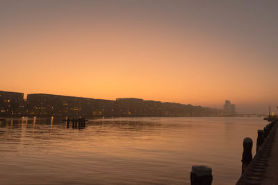 Buildings by river against clear sky during sunset