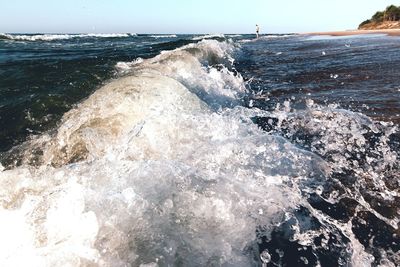 Waves splashing on rocks at shore against sky