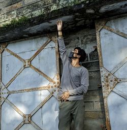 Young man standing against wall touching roof