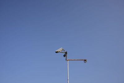 Low angle view of security camera against clear blue sky