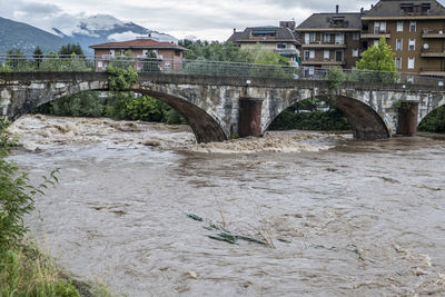 Arch bridge over river amidst buildings against sky