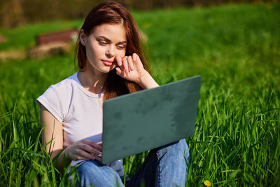 Young woman using laptop while standing on field