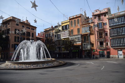 Fountain by street against buildings in city