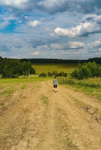 Rear view of teenage girl walking on field against sky