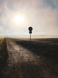 Road sign on field against sky during sunset