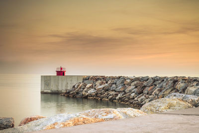 Lighthouse by sea against sky during sunset