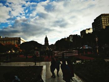 People walking on street amidst buildings in city against sky