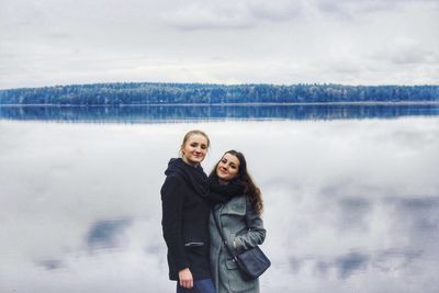 Portrait of smiling friends wearing warm clothing standing against lake