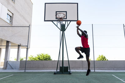 Side view of african american sportsman jumping above ground while playing basketball during training and throwing ball into hoop