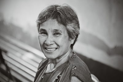 Close-up portrait of smiling senior woman against wall