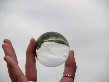 Cropped hand holding crystal ball against sky