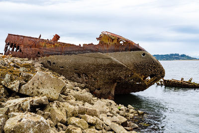 Abandoned boat on rock by sea against sky