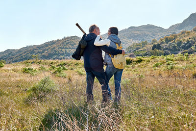 Rear view of a couple hugging while walking through a rural meadow in an autumn or spring pasture. 