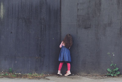 Rear view of girl standing against black wall