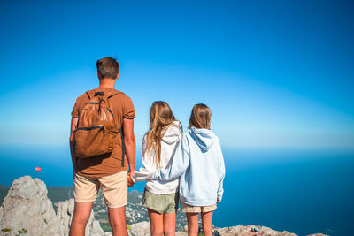 Rear view of people standing by sea against blue sky