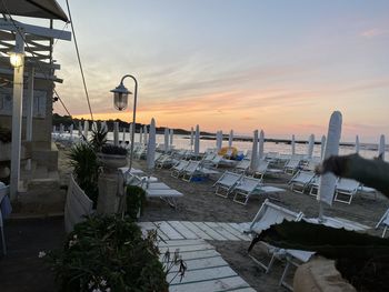 Chairs and table by swimming pool against sky during sunset