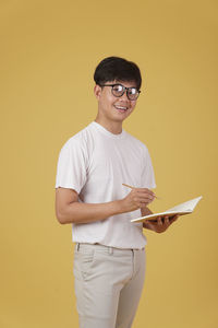 Portrait of smiling young man standing against yellow background