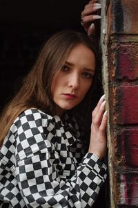 Portrait of a beautiful young woman standing against brick wall