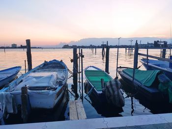 Boats moored at harbor against sky during sunset
